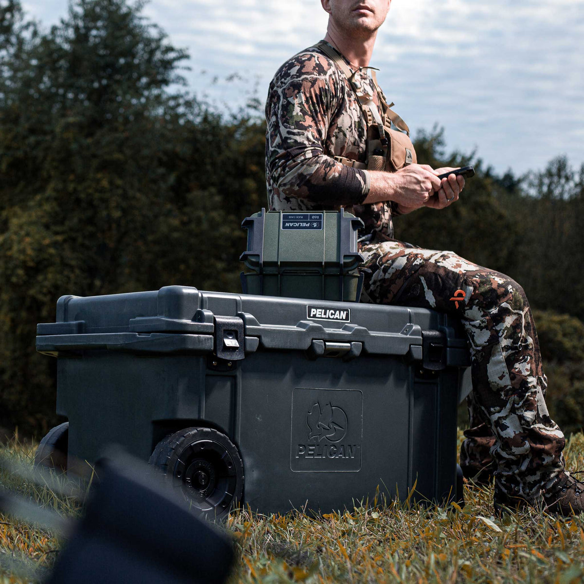 80QW-6-DKGRY Pelican 80QT Elite Wheeled Cooler in charcoal being used as a seat outside during a hunt