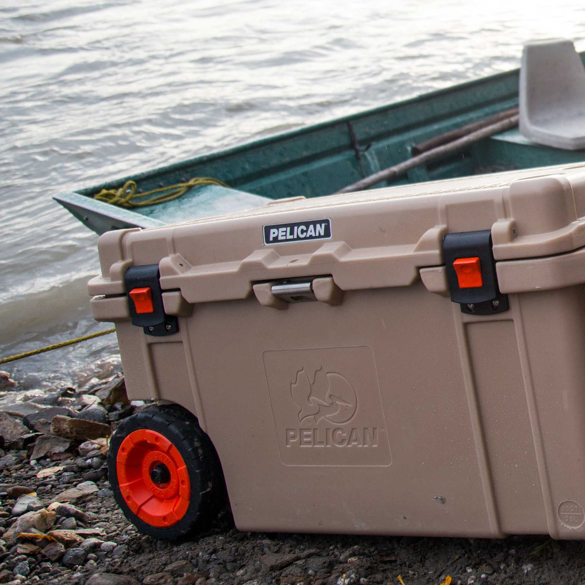 Pelican 80QT Elite Wheeled Cooler in tan being pulled over a rocky beach terrain 