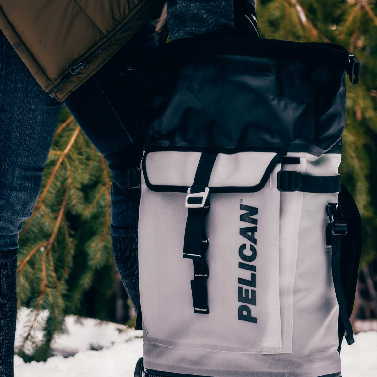 Pelican™ Dayventure Backpack Soft Cooler reaching inside the dry storage compartment outside in the snow