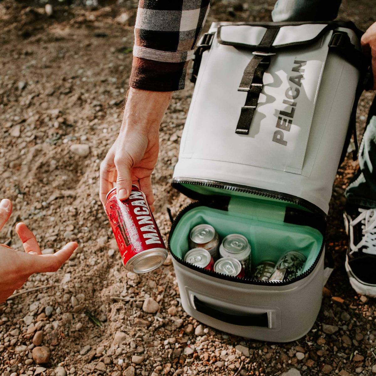 SOFT-CBKPK-LGRY Pelican™ Dayventure Backpack Soft Cooler handing a canned beverage to another person from the cooler compartment